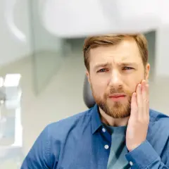 Mężczyzna z bólem zęba trzyma się za policzek. Czy po zatruciu zęba można jeść?