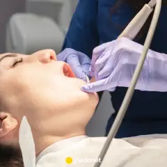 Dentysta w fioletowych rękawiczkach bada ząb pacjentki otwartymi ustami.