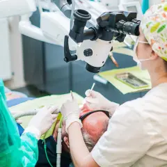 Stomatolog pod mikroskopem aplikuje lekarstwo w zębie pacjenta.