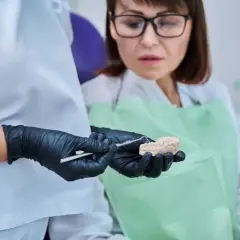 Dentysta pokazuje pacjentce model szczęki, omawiając problem połknięcia plomby amalgamatowej.