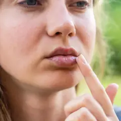 Kobieta aplikuje krem na usta, gdzie widoczne są małe, białe kropki.