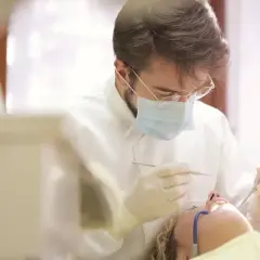 Dentysta w masce i rękawiczkach wykonuje zabieg. Pacjentka leży na fotelu. Pytanie o ile l4 po wyrwaniu ósemki.