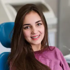 Uśmiechnięta nastolatka z aparatem samoligaturującym w kolorze srebrnym i czerwonym.