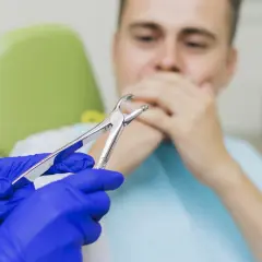 Dentysta w niebieskich rękawiczkach trzyma kleszcze, pacjent zasłania usta. Czy 8 trzeba wyrwac?