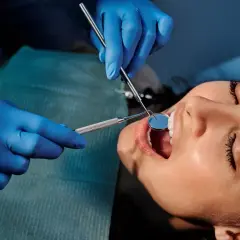 Dentysta bada zęby pacjentki, by wykryć próchnicę. Używa lusterka i narzędzia.
