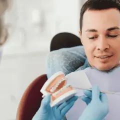 Dentysta pokazuje pacjentowi model szczęki z aparatem, omawiając, czy trzeba usuwać ósemki do aparatu ortodontycznego.