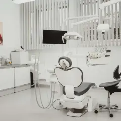Nowoczesny gabinet stomatologiczny i ortodontyczny. Biały fotel dentystyczny, lampa, wiszące narzędzia i obraz z uśmiechem.