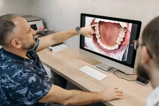 Dentysta pokazuje pacjentowi na ekranie powiększony obraz jamy ustnej, wskazując na zdrową kieszonkę dziąsłową.