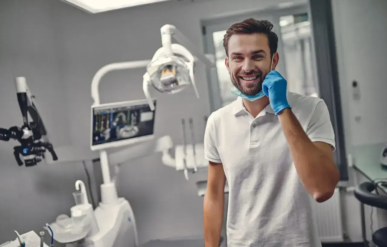 Uśmiechnięty dentysta w gabinecie, gotowy do pracy. Zastanawiasz się, ile trwa plombowanie zęba? Krótka wizyta i zdrowy uśmiech!