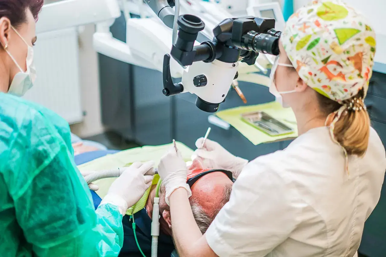 Stomatolog pod mikroskopem aplikuje lekarstwo w zębie pacjenta.
