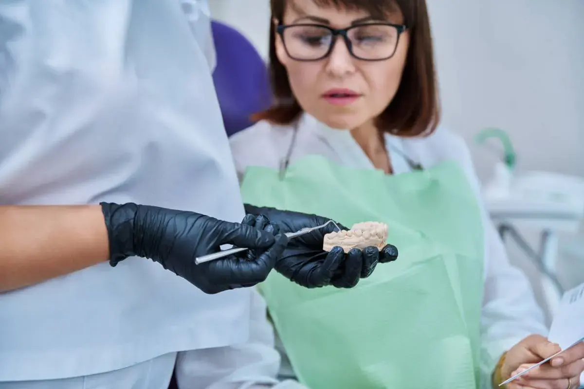 Dentysta pokazuje pacjentce model szczęki, omawiając problem połknięcia plomby amalgamatowej.
