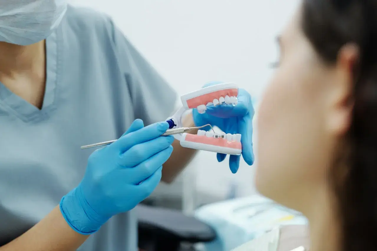 Ortodonta pokazuje pacjentowi model szczęki z aparatem i mikroimplantami ortodontycznymi, wyjaśniając, czy boli.