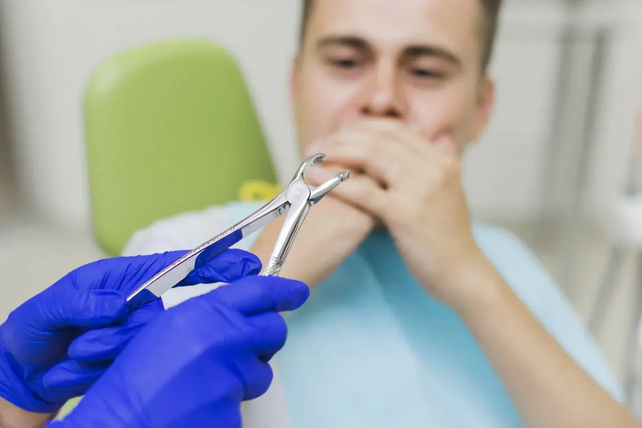 Dentysta w niebieskich rękawiczkach trzyma kleszcze, pacjent zasłania usta. Czy 8 trzeba wyrwac?