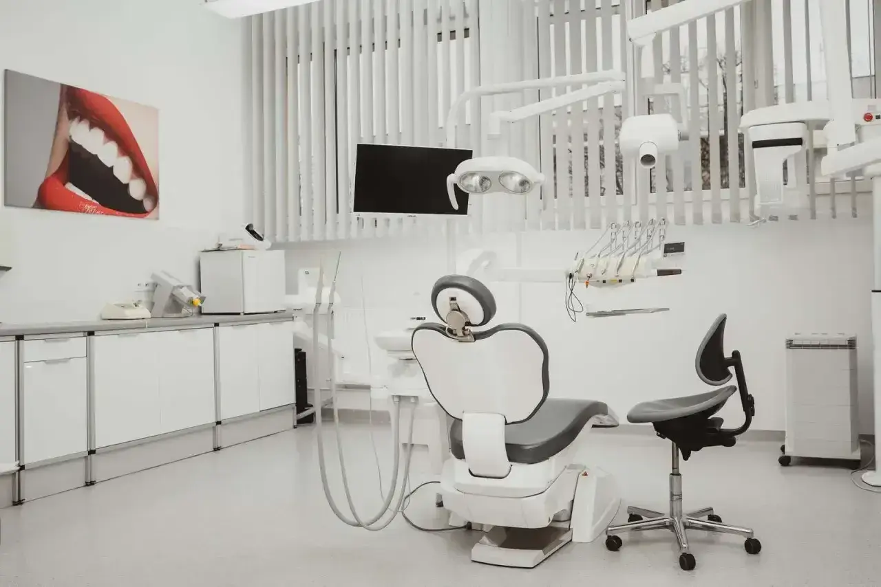 Nowoczesny gabinet stomatologiczny i ortodontyczny. Biały fotel dentystyczny, lampa, wiszące narzędzia i obraz z uśmiechem.