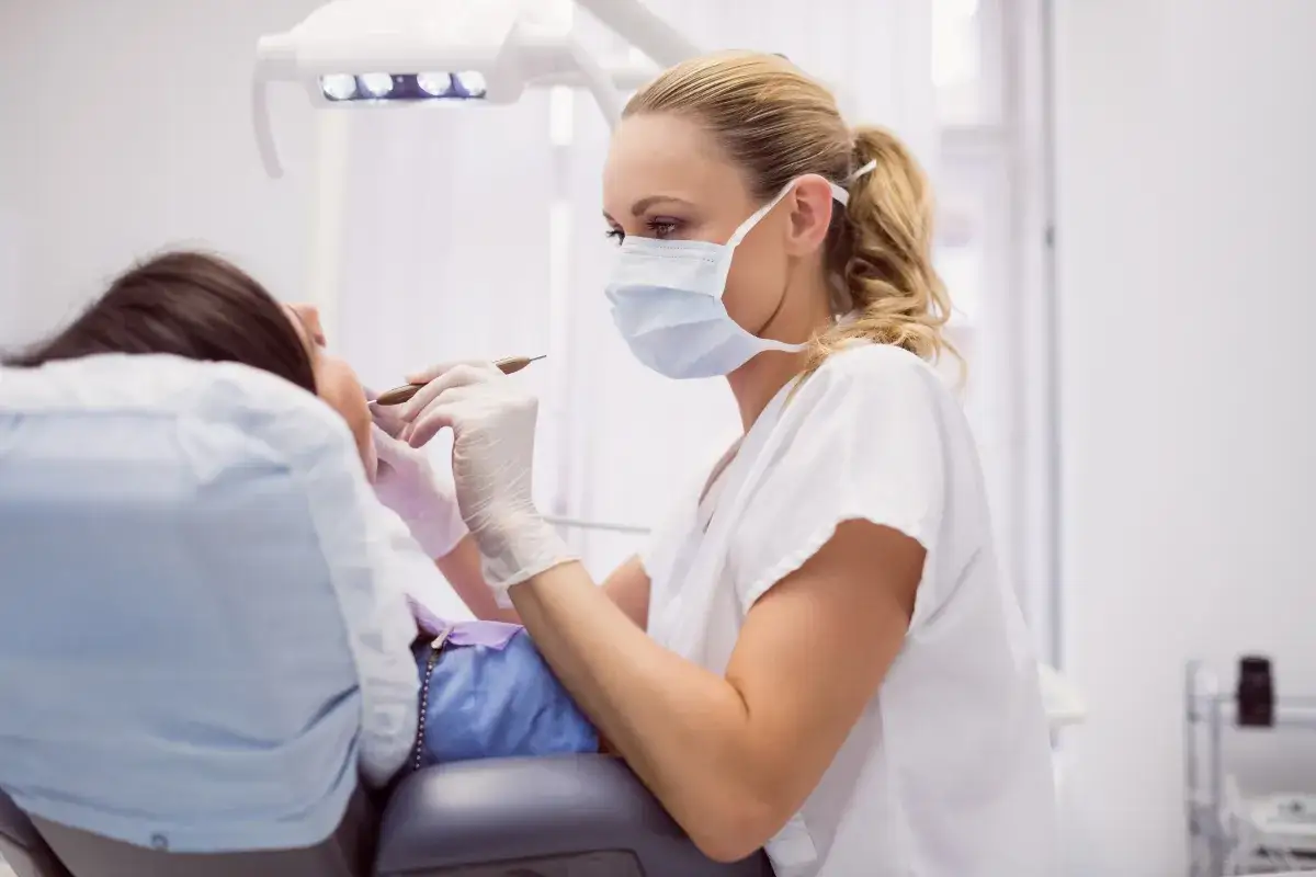 Dentystka w masce i rękawiczkach wykonuje zabieg. Czas potrzebny na plombowanie zęba zależy od wielu czynników.
