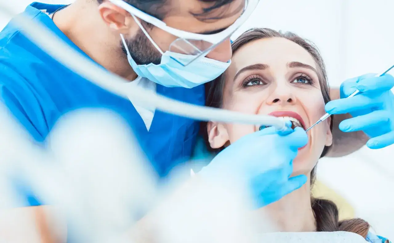 Dentysta w masce i rękawiczkach bada zęby pacjentki. Rozważasz ceny usług stomatologicznych?