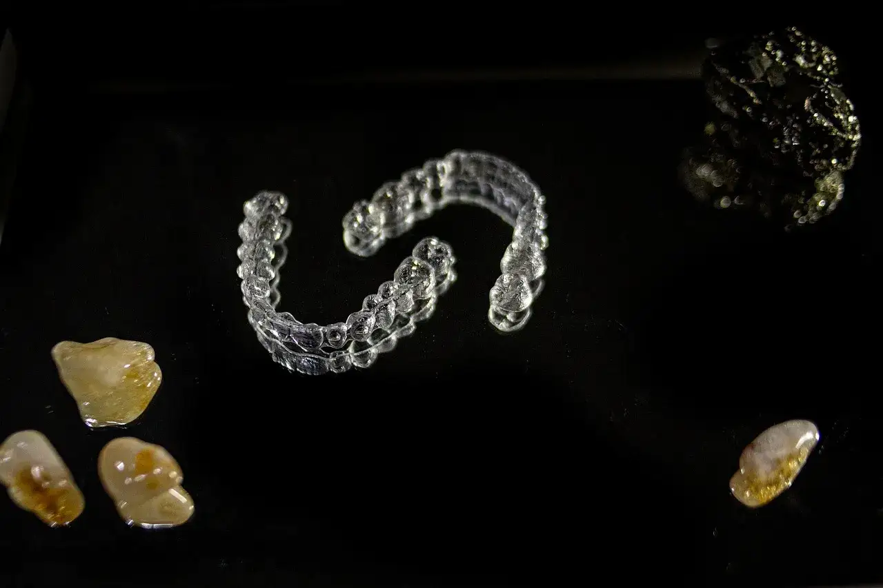 Przezroczyste nakładki Invisalign vs tradycyjny aparat ortodontyczny. Kamienie i błyszczący obiekt na czarnym tle.