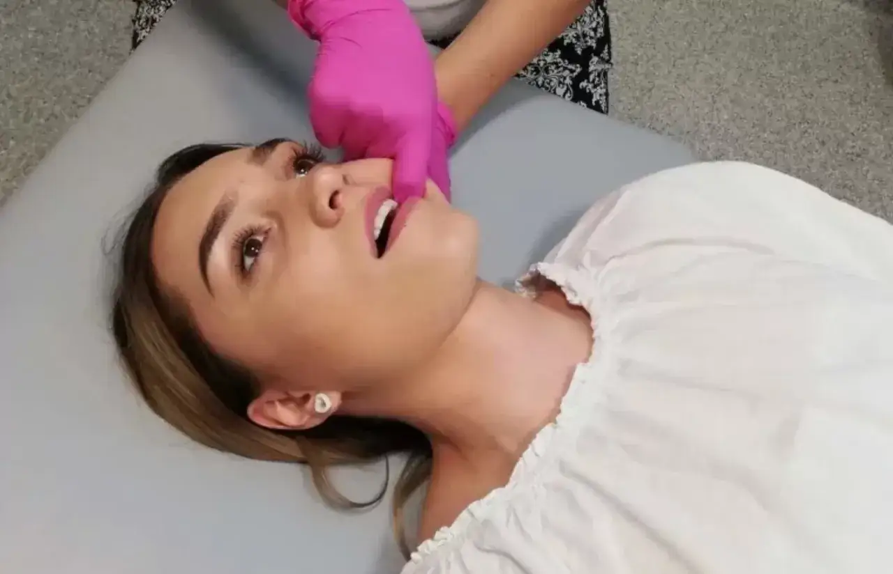 Fizjoterapeuta stomatologiczny w różowych rękawiczkach delikatnie dotyka ust pacjentki.