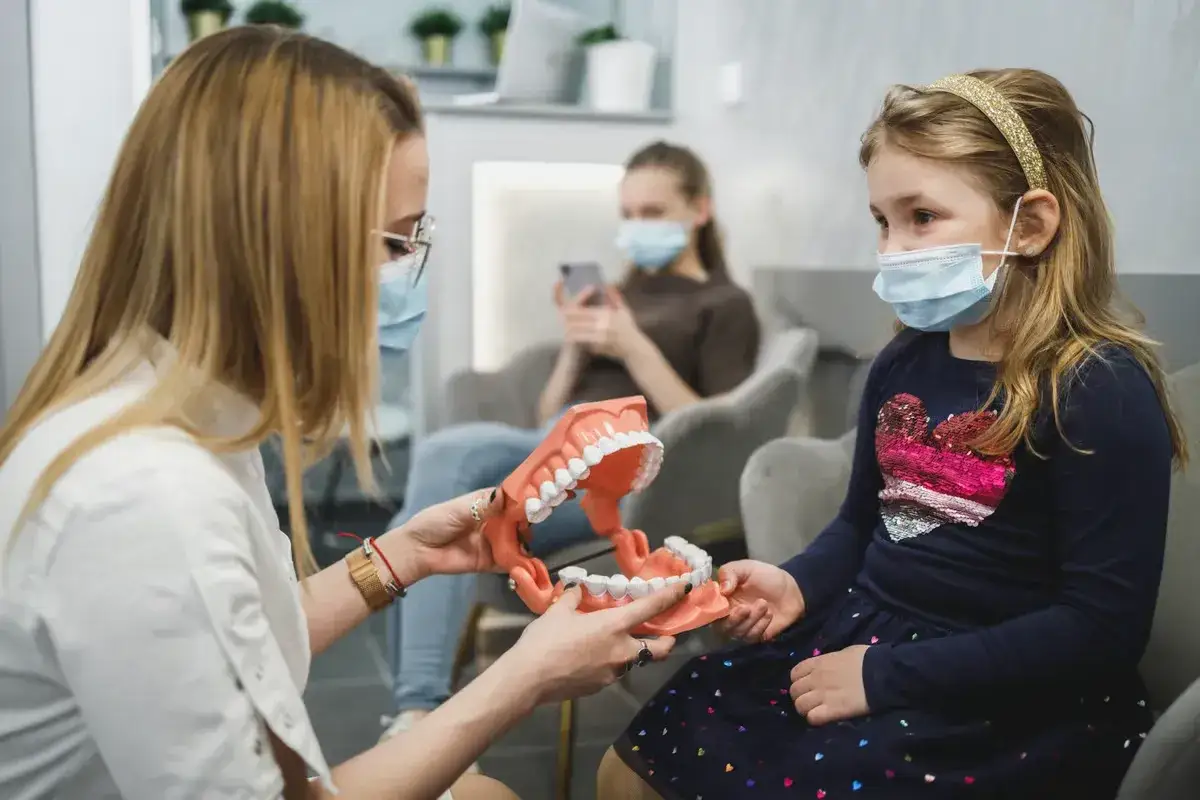 Kiedy z dzieckiem do ortodonty. Lekarka pokazuje model szczęki małej pacjentce, która czeka na wizytę.